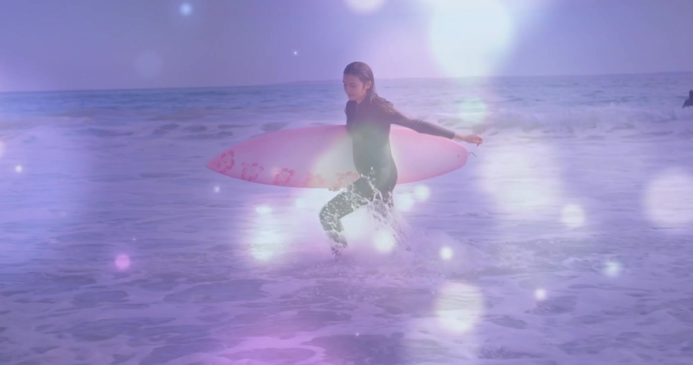 Donna surfista che si addentra tra le onde, camminando più in profondità, regolando la tavola rosa e preparandosi a surfare sotto un effetto bokeh