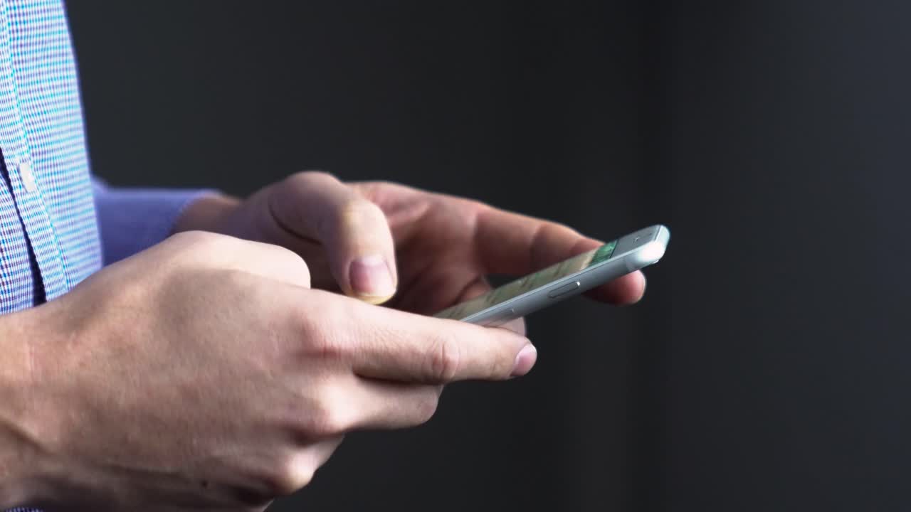 Close up side ways shot of a man typing on cellphone, fingers on touch screen