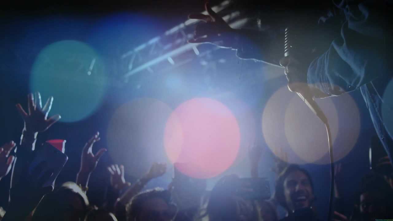 Vocalista che si sporge dal palco del concerto, raggiungendo il microfono, con cavo, telefoni alzati, tazza rossa in alto e bagliori che si disperdono.