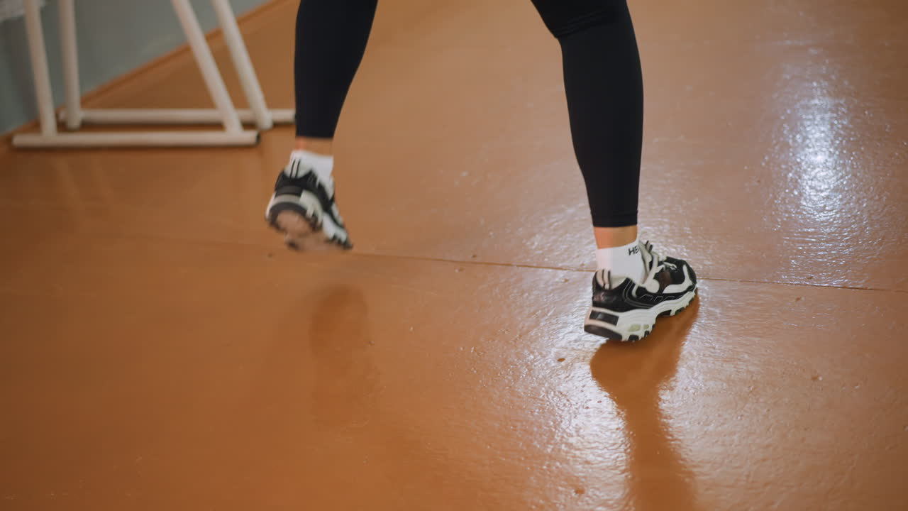 Leg view of lady in black tights and canvas sneakers dancing and jumping with energy in studio showing expressive athletic motion rhythm fitness activity dynamic training movement