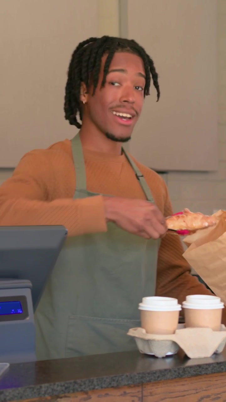 Vertical video: Packing green apron barista placing cups at counter and filling bag after POS order
