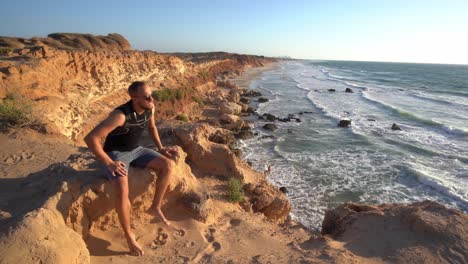 A-man-walking-towards-the-edge-of-a-cliff-and-watching-the-amazing-sunset-near-a-beach-at-Hadera,-Israel