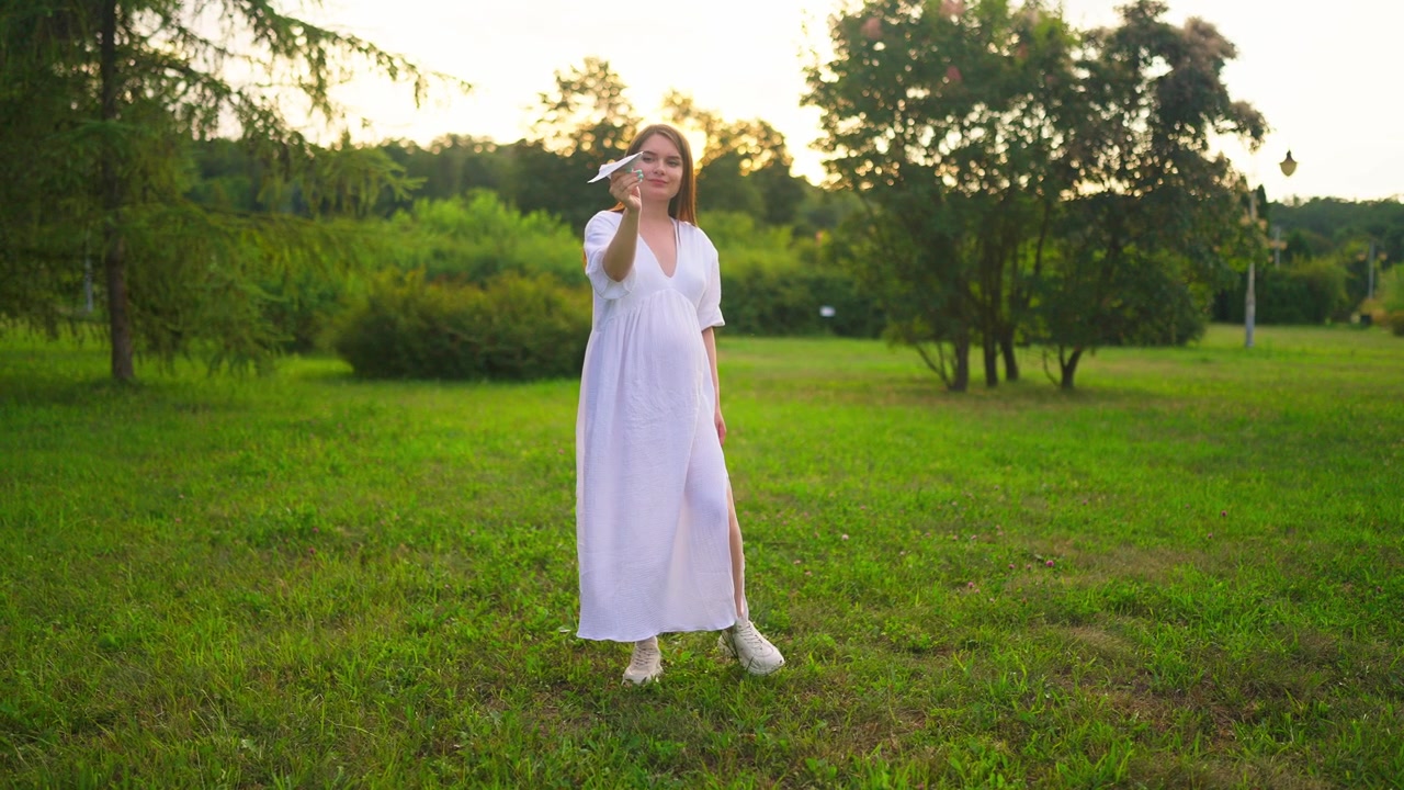 Donna incinta felice che tiene un aeroplano di carta in un parco verde.