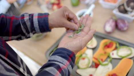 Midsection-of-senior-african-american-man-cooking,-seasoning-vegetables-in-kitchen,-slow-motion