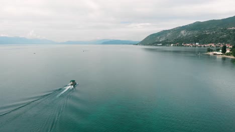 Aerial-shot-following-boat-at-Ohrid-Lake-in-Mcedonia-with-view-of-coast,-clif-and-beautiful-blue-water