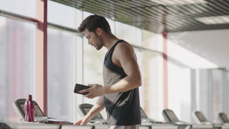 hombre atleta hablando por teléfono móvil en la cinta de correr en el club de fitness.