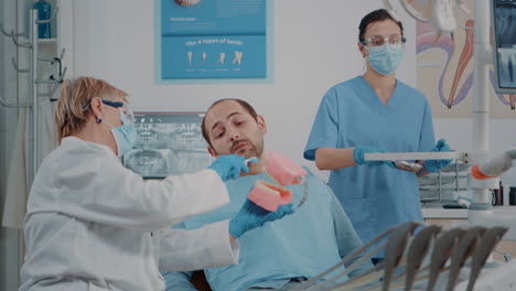 stomatologist using artificial jaw to explain correct way to brush teeth