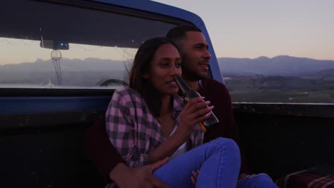 young couple on a road trip sitting outside on their truck at dusk