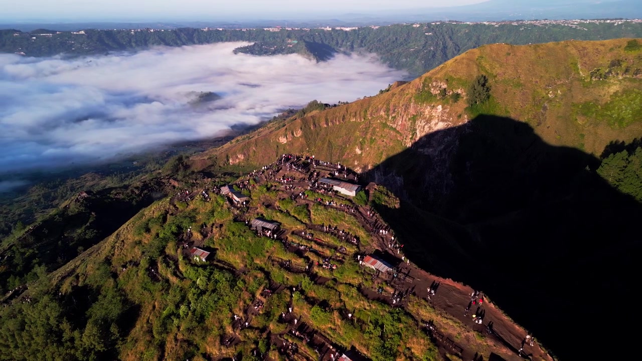 Punto panoramico sulla cima della montagna con escursionisti all'alba sopra un mare di nuvole su un paesaggio vulcanico con cratere nella luce dell'ora d'oro, ampio filmato aereo con drone