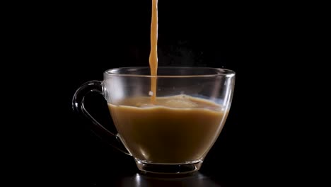milk streams into a glass cup of coffee, creating a swirling effect against a dark backdrop