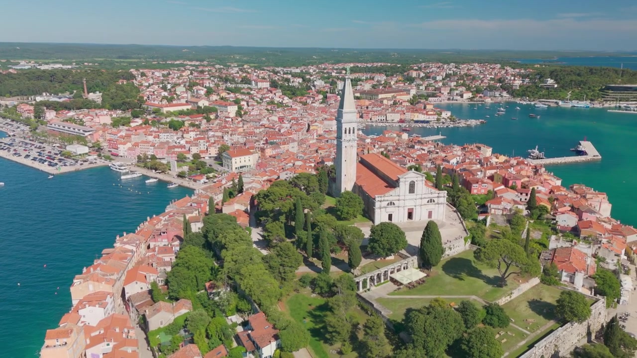 Drönare som cirklar runt Sankta Eufemia i Rovinj, med kyrkan och den gröna parken på kullen i centrum, en yacht på Adriatiska havet och gamla stan som breder ut sig bakom.