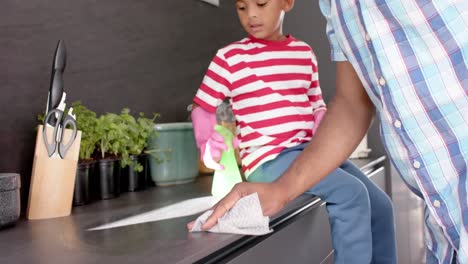 African-american-father-and-son-cleaning-countertop-and-doing-high-five-in-kitchen,-slow-motion