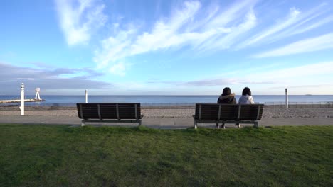 scenic view of girls sitting and talking on a bench and looking at the beach, wide static