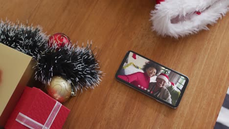 African-american-mother-and-daughter-wearing-santa-hats-on-christmas-video-call-on-smartphone