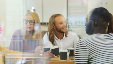 camera focuses on a multiethnic group of friends through the window talking sitting at a table in a cafe