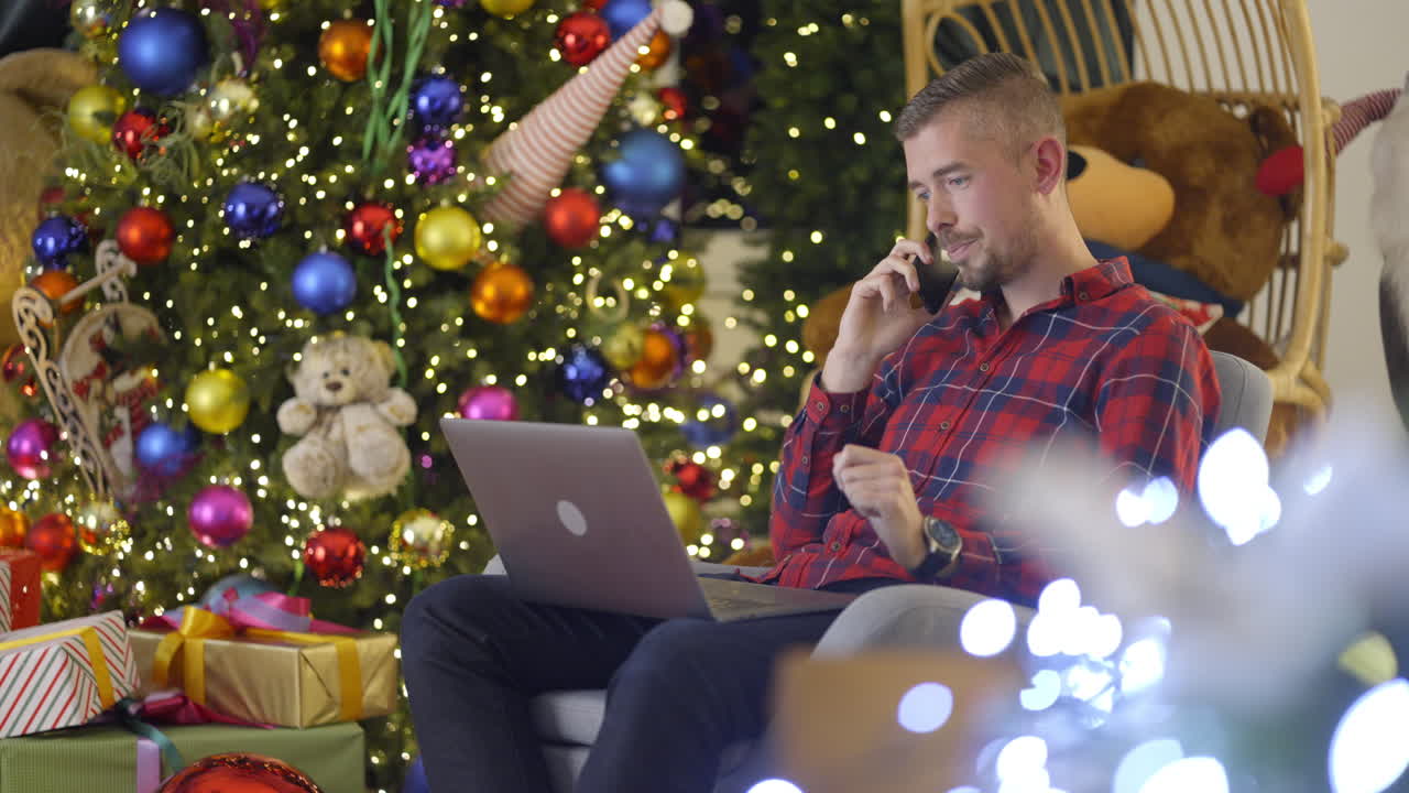 Man working on laptop and talking on phone near Christmas tree