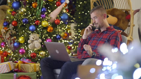 man working on laptop and talking on phone near christmas tree