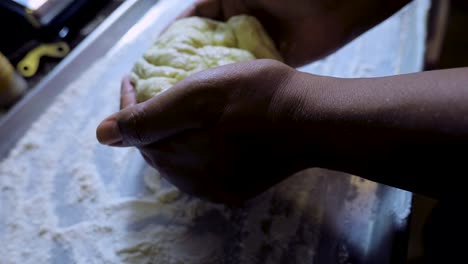 close up view of african american woman's hands kneading pizza dough in a silver pan in slow motion