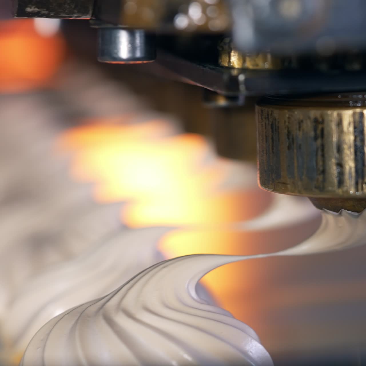 Whipped white vanilla cream comes out off a metal nozzle. Freshly squeezed marshmallows on the conveyor belt. Close up