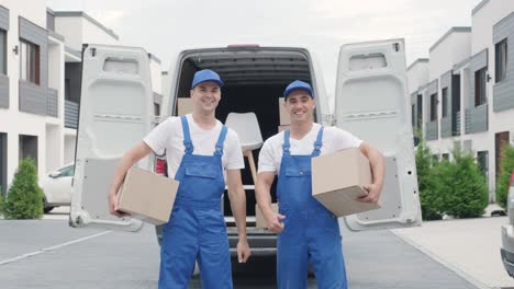 two young workers of removal company unload boxes from minibus into customer's home