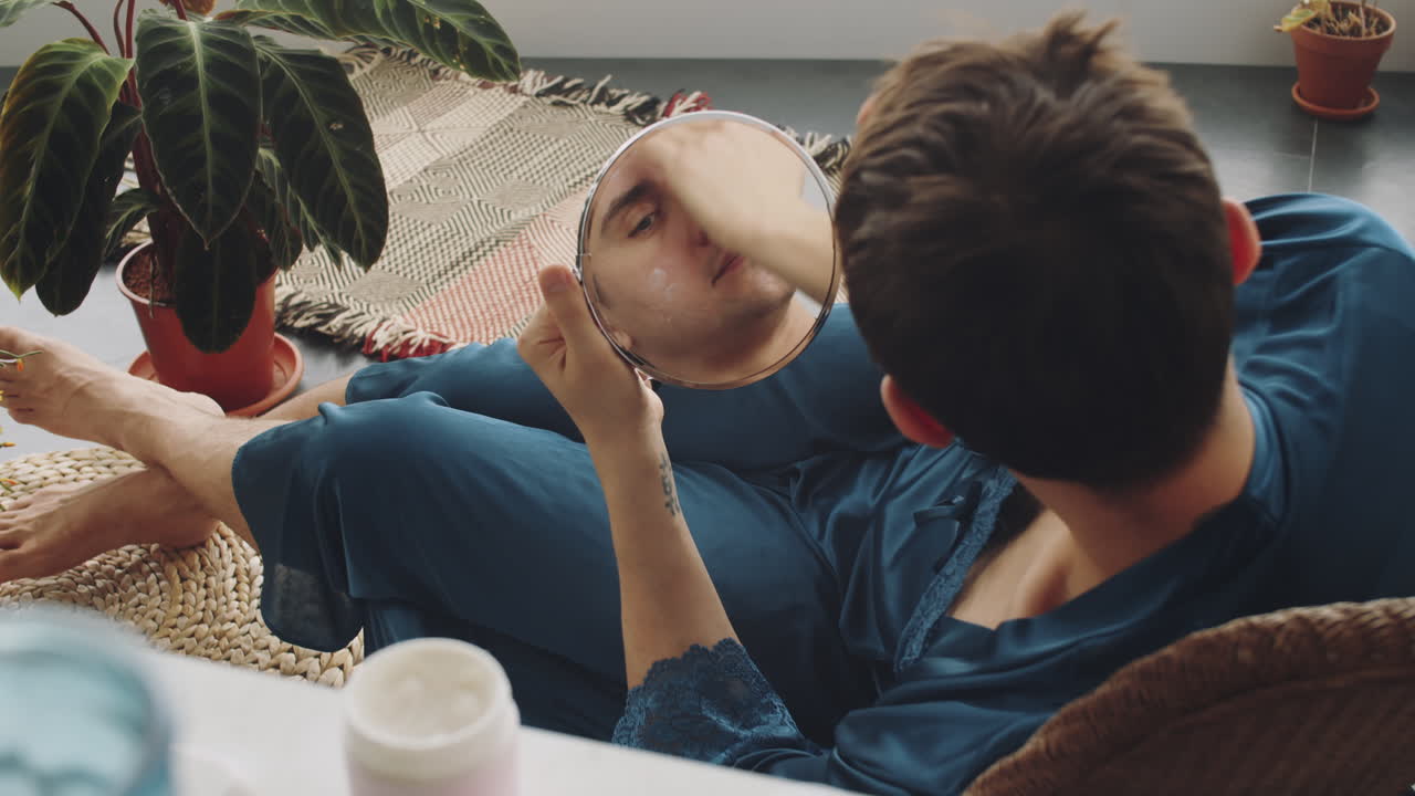 트랜스젠더 남자가 집에서 얼굴에 크림을 바르고 있습니다.