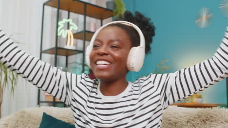 african american woman girl enjoying listening music dancing on sofa wireless headphones at home