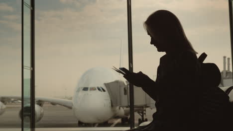 Silueta-De-Una-Mujer-Con-Documentos-De-Embarque-De-Pie-En-La-Ventana-De-La-Terminal-Fuera-De-La-Ventana-Ab