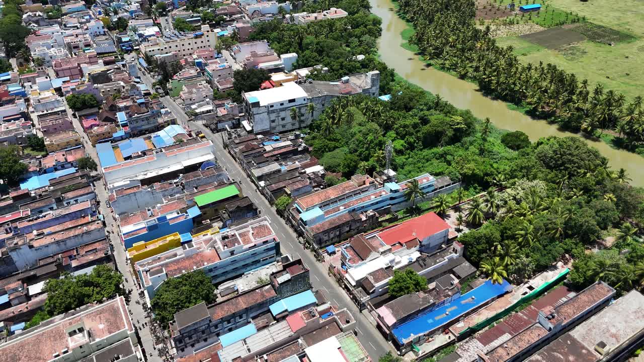 Aerial view of Tenkasi town, highlighting its dense layout of houses and buildings interspersed with greenery. In the distance, lush fields and water bodies are visible