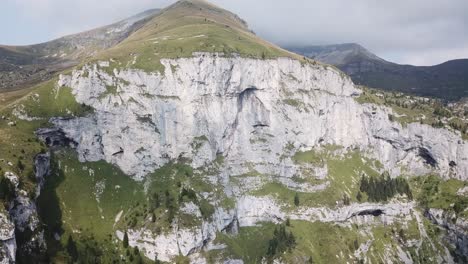 big white cliff of in italian dolomites with overcast weather in the background and green fields on top