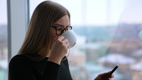 beautiful woman wearing eyeglasses using cellphone and drinking coffee