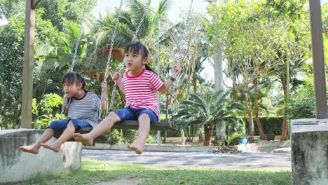 cute little sisters are playing on swing in the outdoor playground in the park. play is learning in childhood.