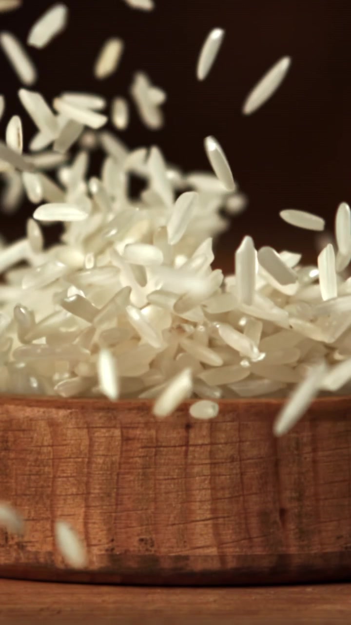 Chicchi di riso bianco che cadono in una ciotola di legno al rallentatore