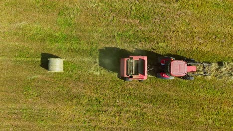 slow motion shot of fresh hay bale ejected by red tractor in open meadow