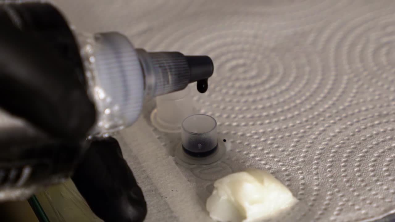 클라이언트 세션을 준비하기 위해 작은 용기에 검은 잉크를 첨가하는 문신 아티스트의 느린 동작 클로즈업 드