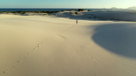 drone shot chasing a man walking alone on sand dunes