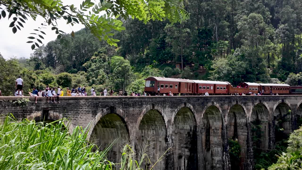 Scenic view of a red train over the iconic nine arches bridge, surrounded by lush green forest in demodara near ella, sri lanka