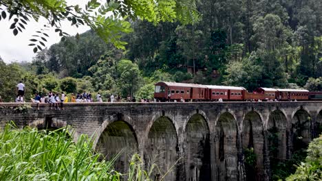 scenic view of a red train over the iconic nine arches bridge, surrounded by lush green forest in demodara near ella, sri lanka