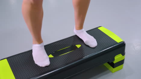 close-up of person legs in white socks stepping onto and off workout bench during fitness routine, reflection on polished gym floor adds depth to dynamic movement and controlled step exercise