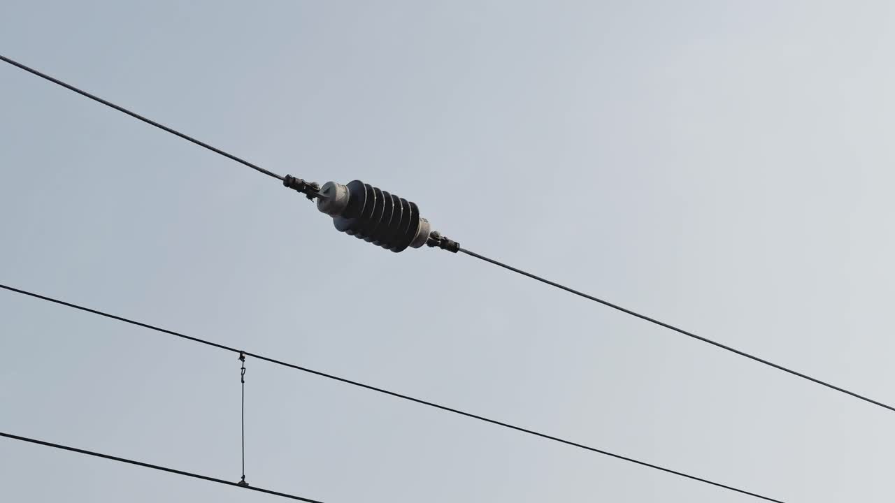 Closeup of ceramic insulator mounted on overhead railway electric wire, isolating high voltage traction line against clear sky, showing power infrastructure detail