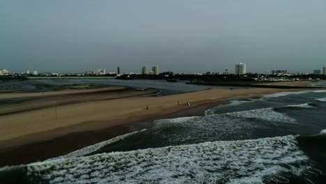 Drone-footage-of-Beach-with-a-backwater-opening-to-it-with-a-city-skyline-with-high-rises-in-backdrop