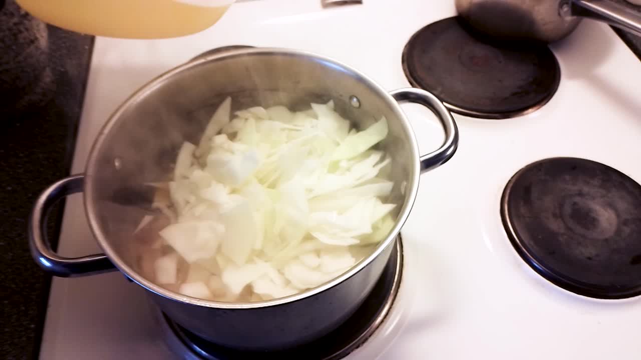 Male hand is adding cut white cabbage, potatoes, and leek to the soup - Cooking Pork Cabbage Soup