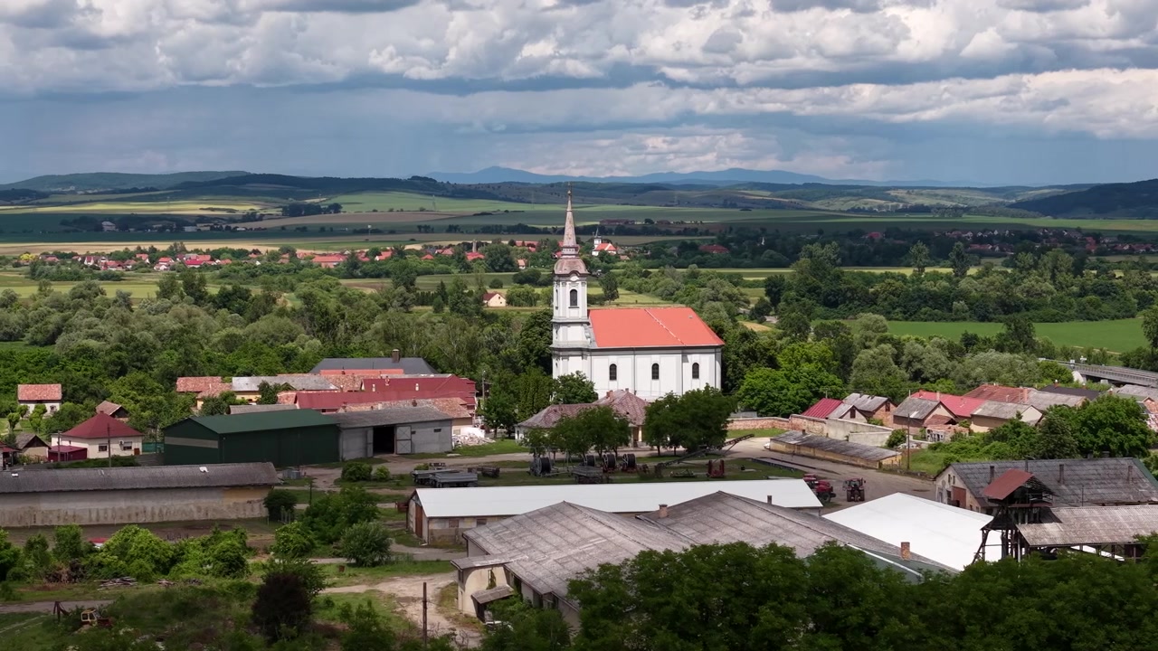 Eine malerische Luftaufnahme zeigt eine traditionelle Kirche in einem kleinen ungarischen Dorf, umgeben von grünen Feldern und sanften Hügeln