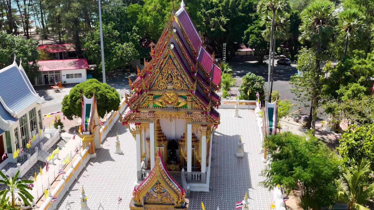 Aerial view of a temple with a vibrant roof surrounded by trees and a courtyard in daylight.