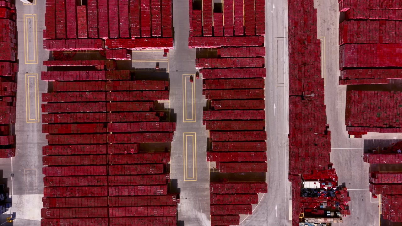 Top-down view of a large outdoor storage yard filled with rows of red stacked beverage crates organized in uniform blocks with marked lanes between them