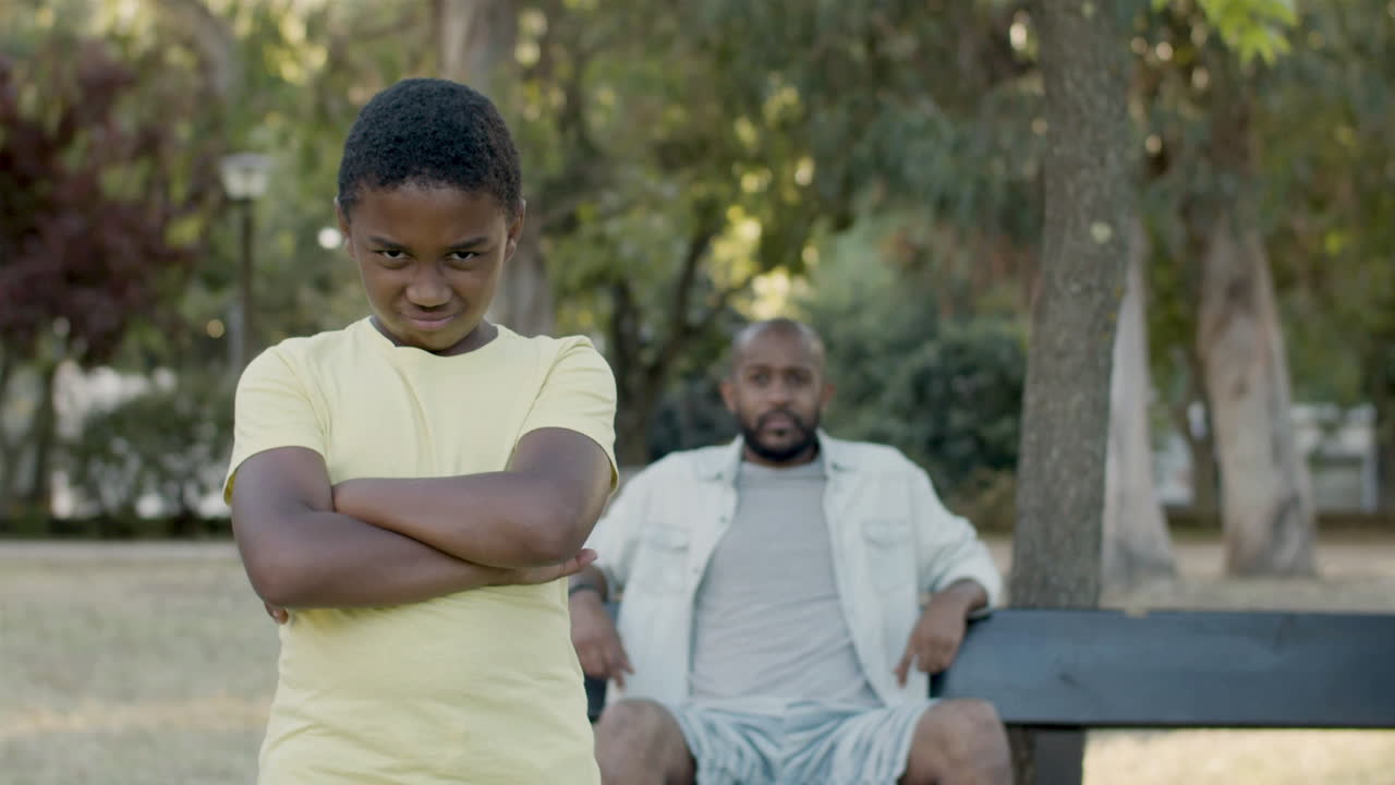 Young black boy posing at camera, folding arms and frowning.