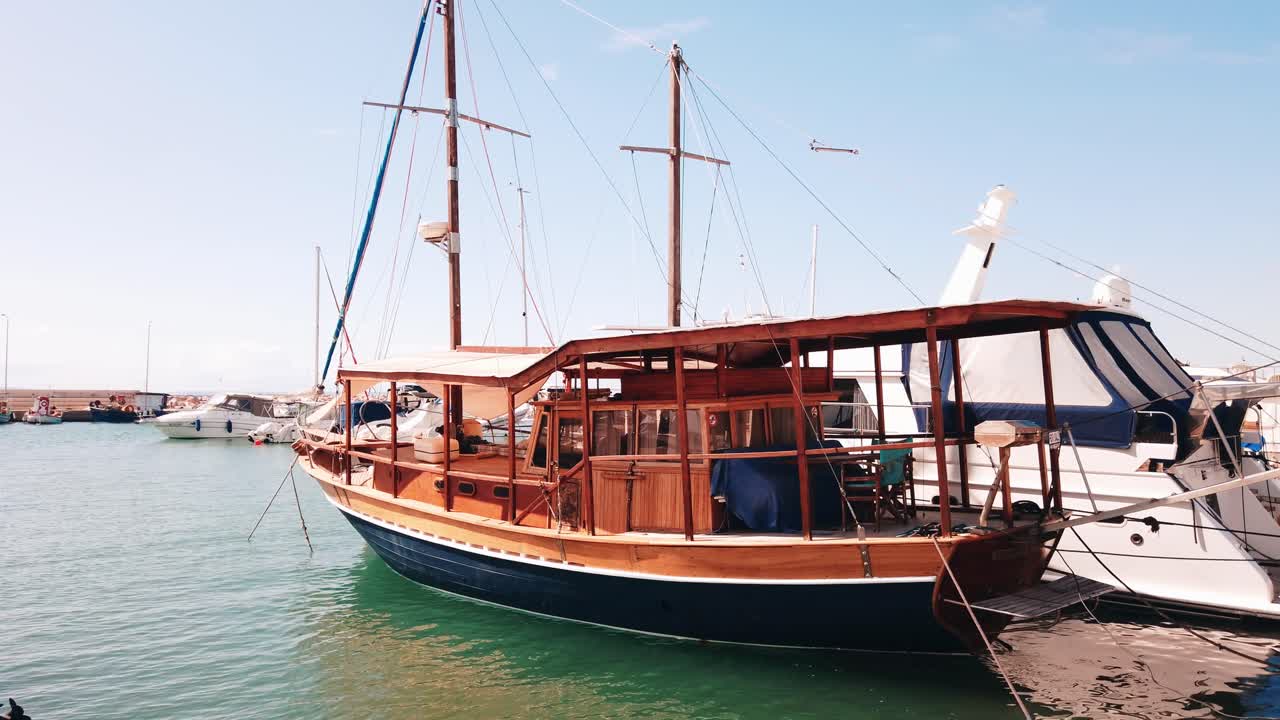 Moored vintage sailboat in Aegean sea port, made of wood, yachts around. Slow motion