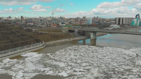 Malerischer-Fluss-Mit-Eis-Vor-Modernen-Stadtgebäuden