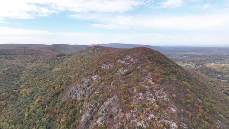 an aerial view high over storm king mountain in upstate ny during the fall foliage change, on a beautiful day with white clouds