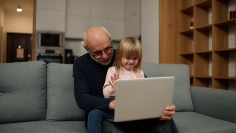 Grandfather-and-small-granddaughter-having-video-call-together-using-laptop