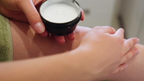 close-up view of hands holding black container with cream, applying cream to knee, part of skincare routine, moisturizing, rejuvenating, smooth skin, body care, healthy skin, self-care moment